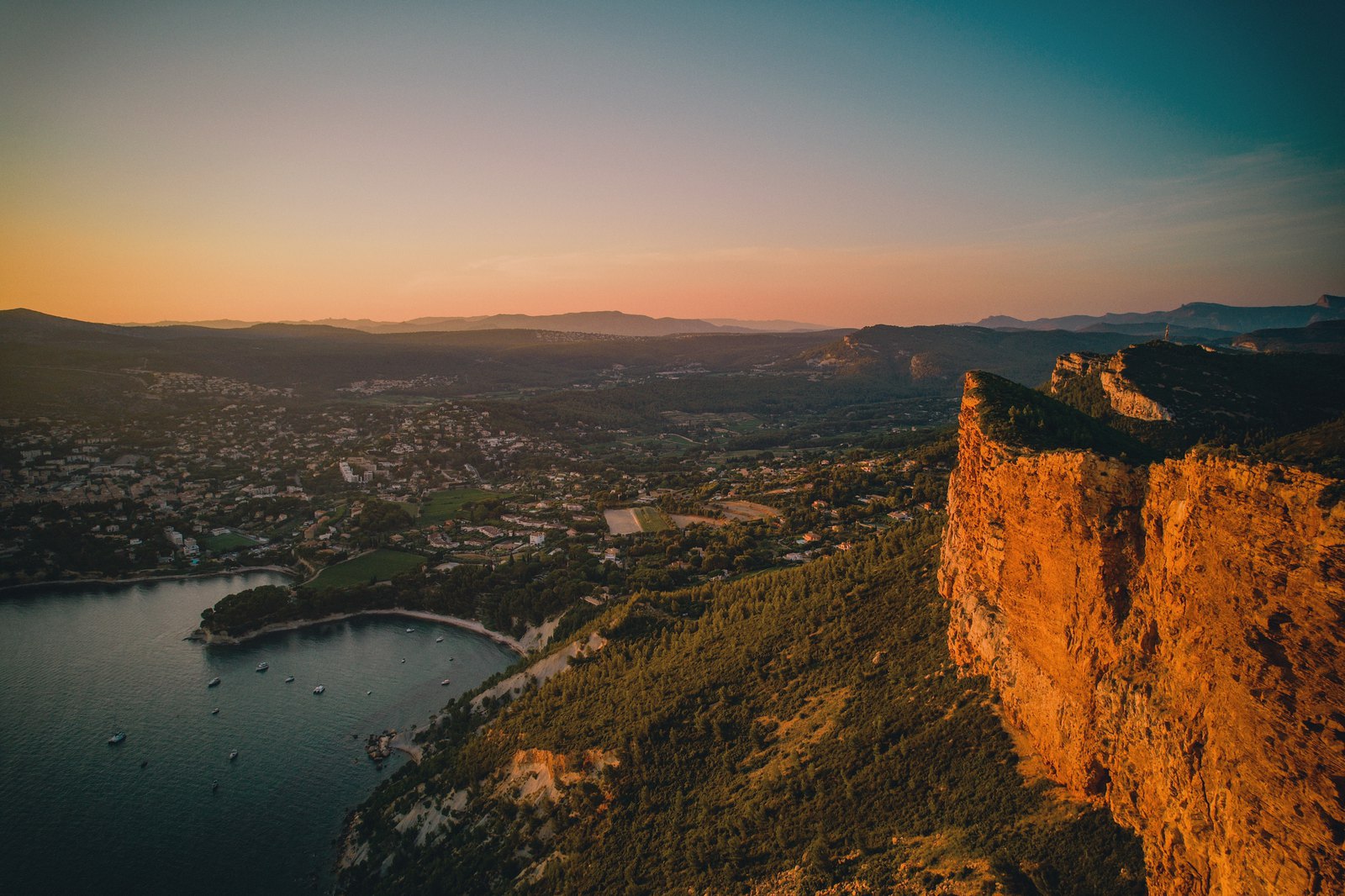 Harbor town and bay at dusk beside a glowing orange cliff