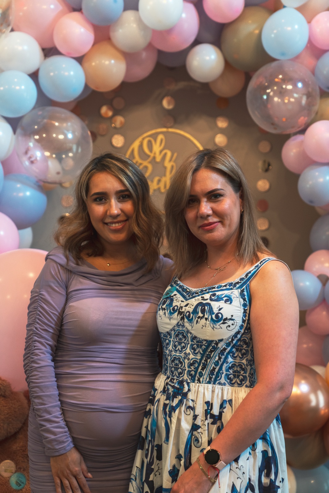 Two women in front of a pastel balloon arch