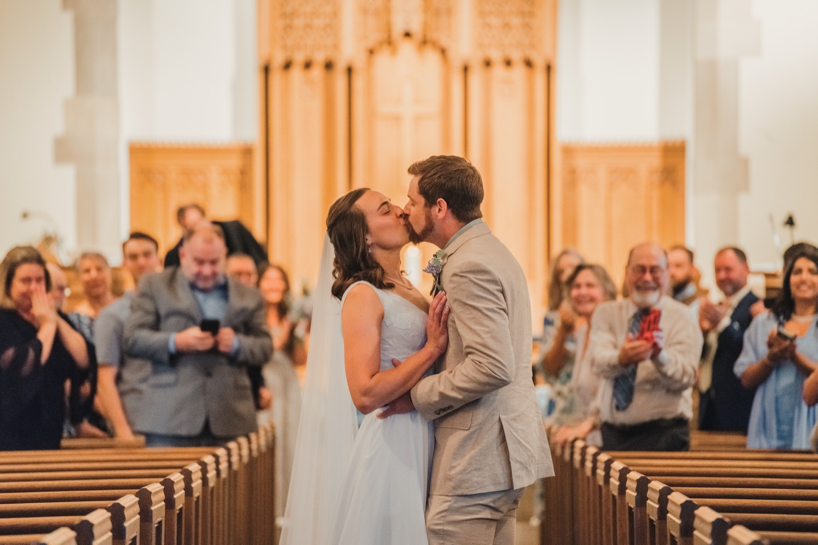 Couple kissing in the church aisle as guests cheer